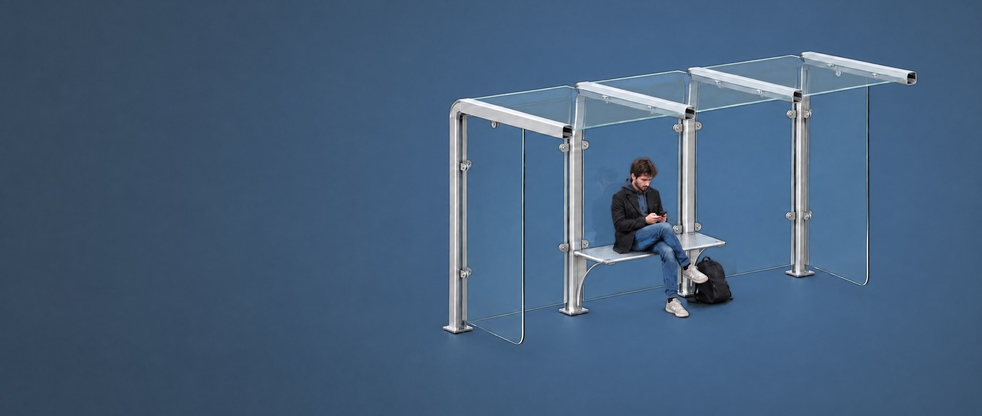 Bus shelter with an aluminium frame and glass panels, with someone sitting on the seat between the two middle posts